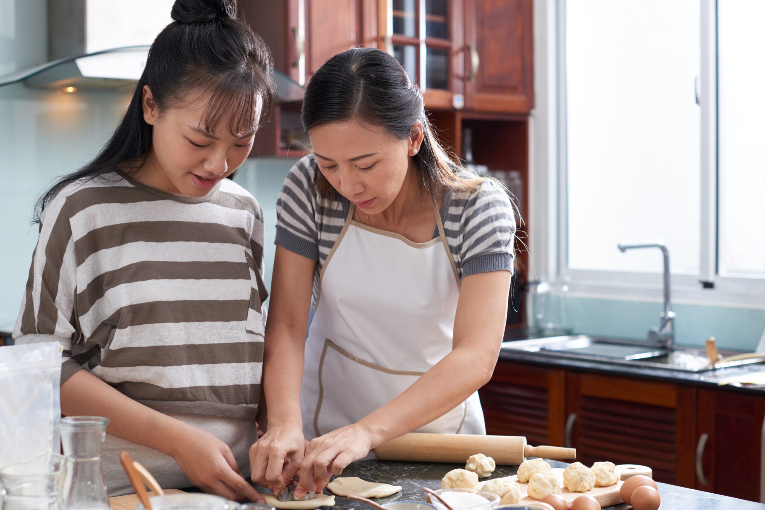 two young asian women cutting out cookies from dough kitchen counter 1 scaled